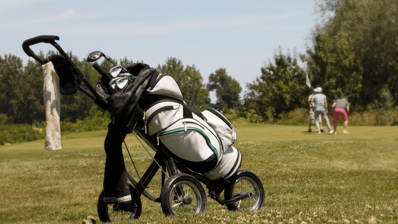 Golf Push Cart Accessories is the focus of this picture. Golfers are in the distance finishing putting on a hole.