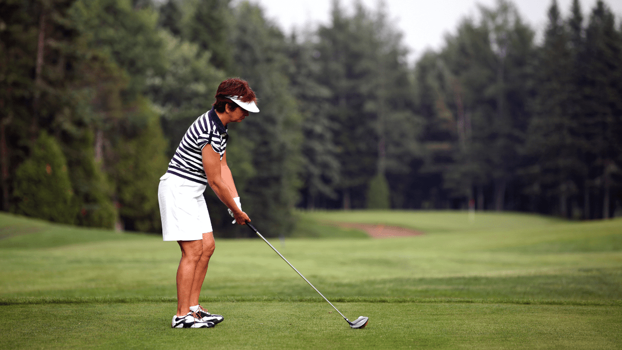 article - best drivers for senior women, and shows senior woman hitting her driver off the tee. Wearing white shorts, white hat, and dark brown hair.