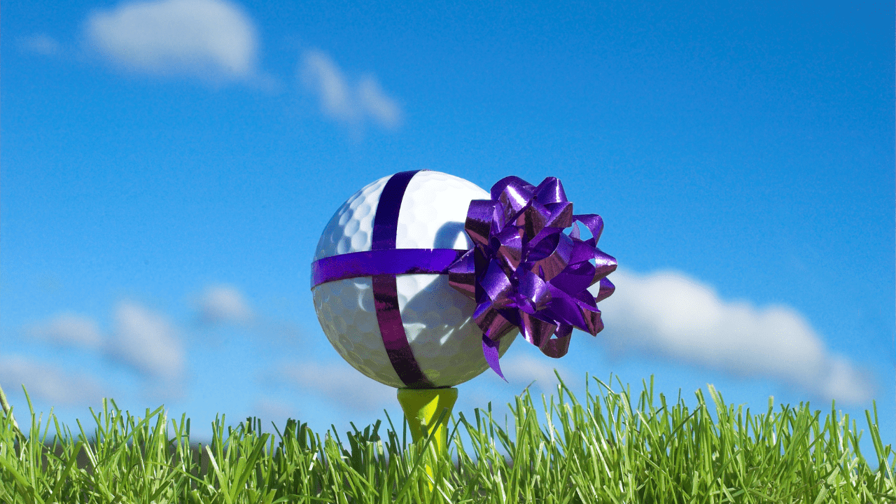 personalized golf gifts can't get more unique that this photo with a purple bow wrapped around a ball on a tee.