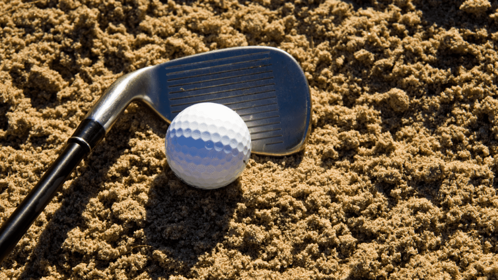 Golf Wedge Degrees article shows wedge in sand trap with a golf ball next to it.  Close up club head view.  