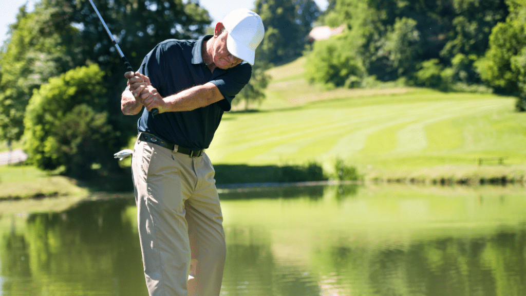 senior hitting his golf ball over a pond.