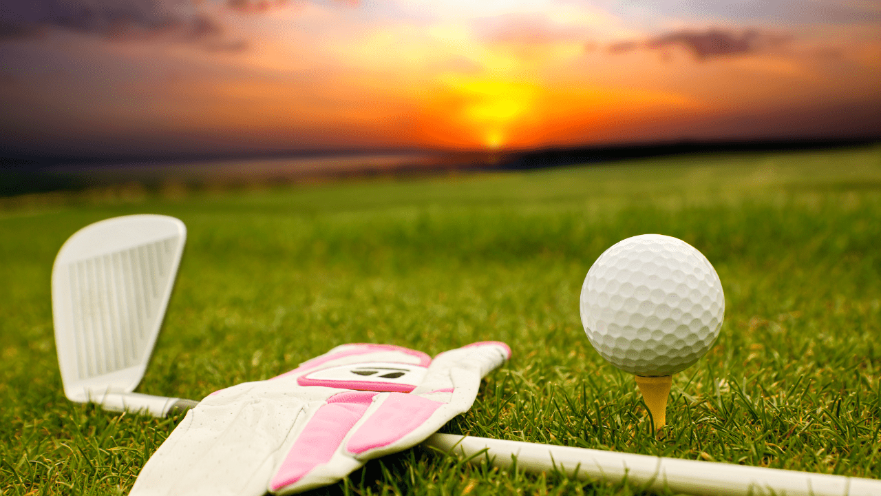 Picture shows a beautiful sunset with a golf ball, golf club, and golf glove.