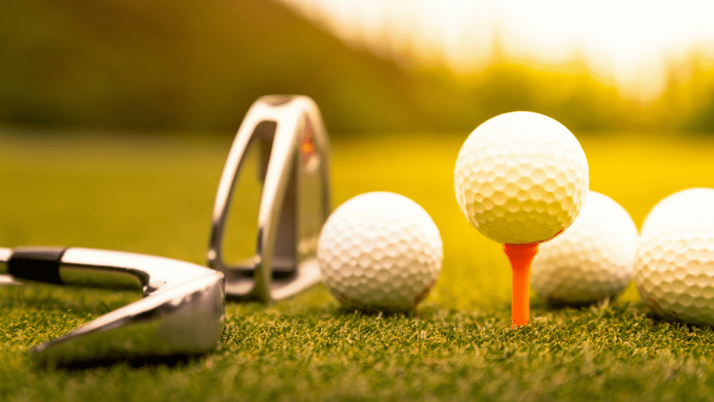 sunset photo of golf balls, golf tee, and golf iron up close.