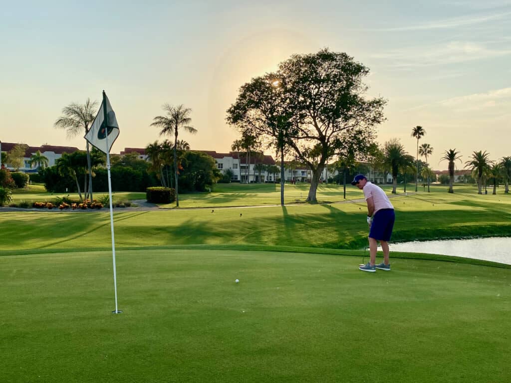 male golfer on the putting green mid-shot with sunset int the distance.