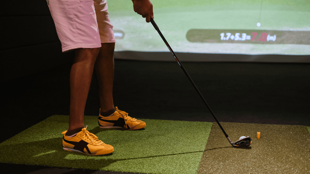man hitting at a screen with golf simulator - only showing feet and clubhead.