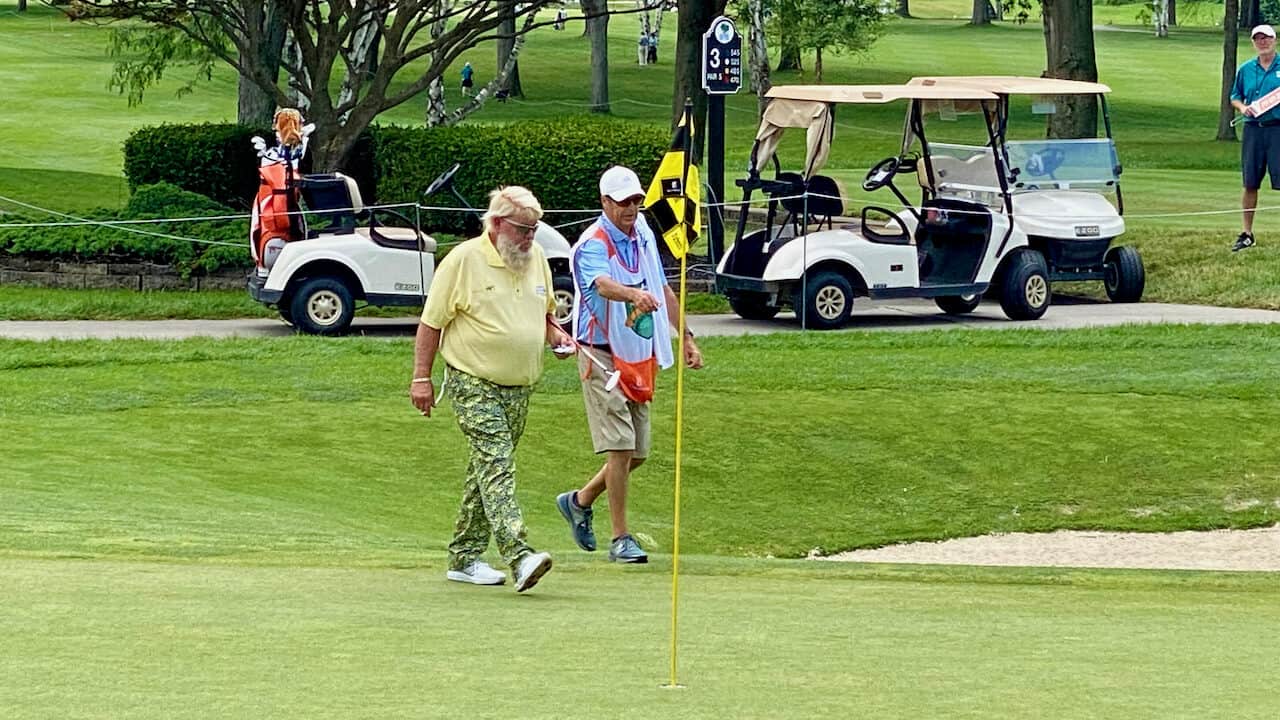 John Daly putter in hand walking with his caddie on the En-Joie Golf Club course.
